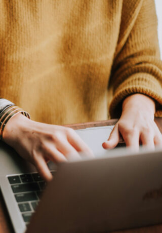 Person in orange jumper typing on laptop